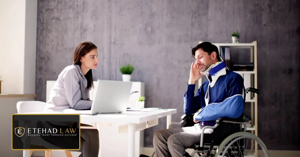 Injured man in a wheelchair with a neck brace consulting a legal professional at a desk – Etehad Law.