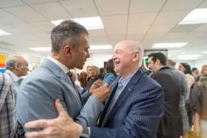 Two guests greeting each other in a crowded room at the grand opening