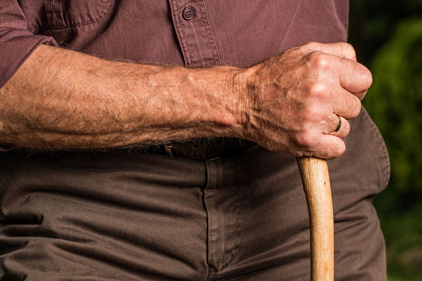 Close-up of an elderly nursing home resident's hand gripping a wooden cane